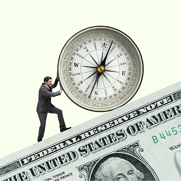 A businessman pushing a compass while scaling a dollar bill like a mountain.