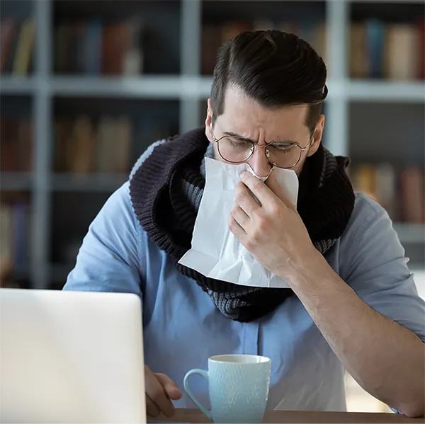 A professionally-dressed person wearing a cowl scarf and blowing their nose.