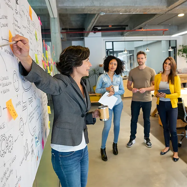 A group of professionals watching their colleague give a presentation in front of a whiteboard.