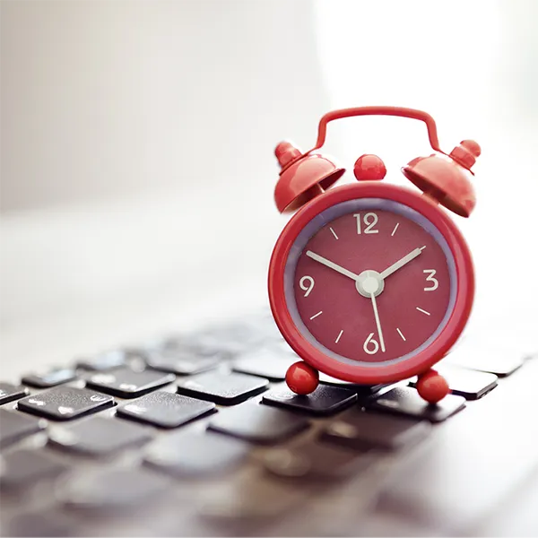 A red alarm clock rests on top of a computer keyboard.
