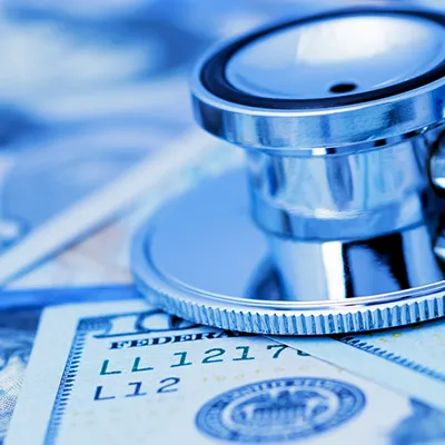 A stethoscope laying across scattered 100 dollar bills.