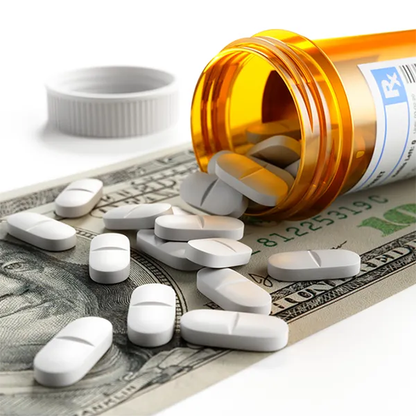 A prescription bottle on its side, spilling pills across a 100 dollar bill.