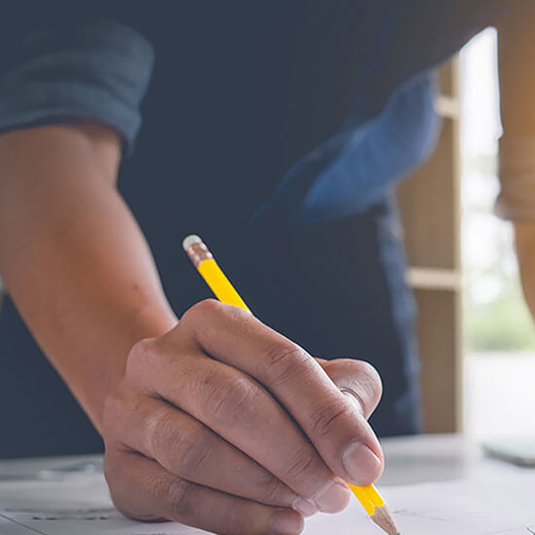 A contractor making notes with a pencil. There are tools and a hard hat in the background.