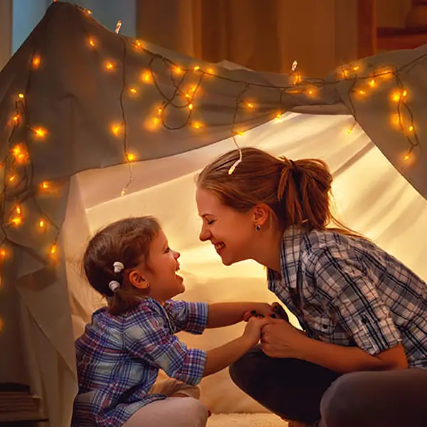 A mom and her daughter smiling and laughing in a blanket fort.