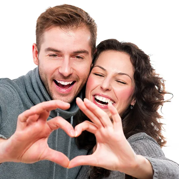 A couple smiling and making a heart with their fingers.