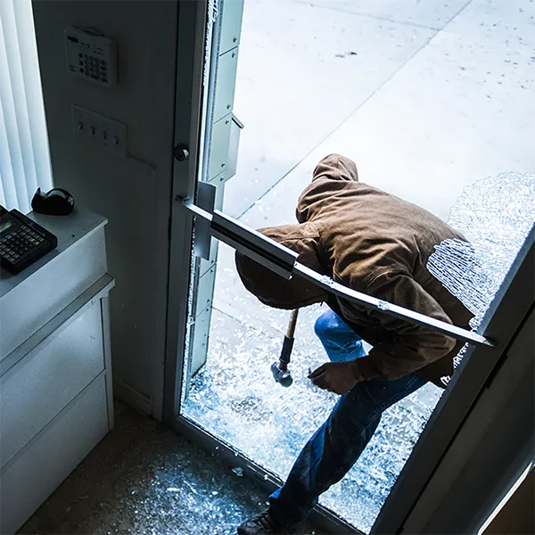 A person wearing a jacket breaking the front door of a business with a hammer.