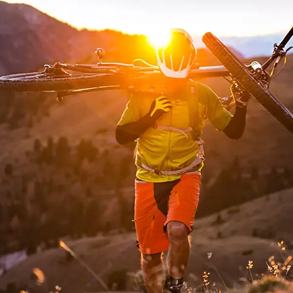 A cyclist walking up a mountain carrying their bike over their shoulder.