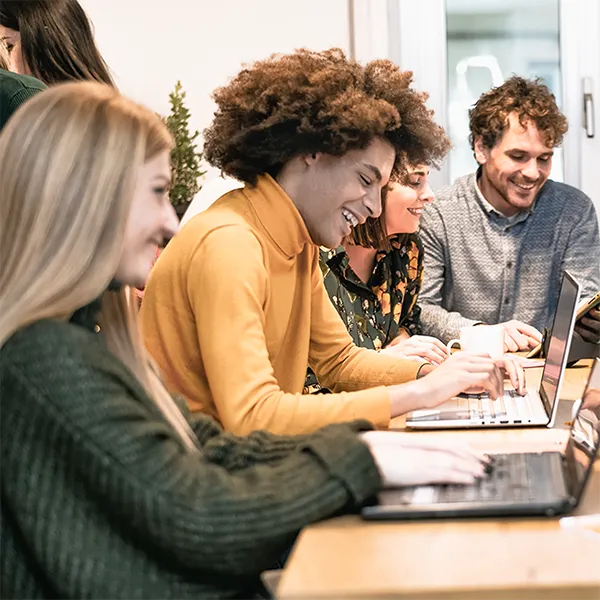 A group of young professionals talking and laughing while working at their computers.