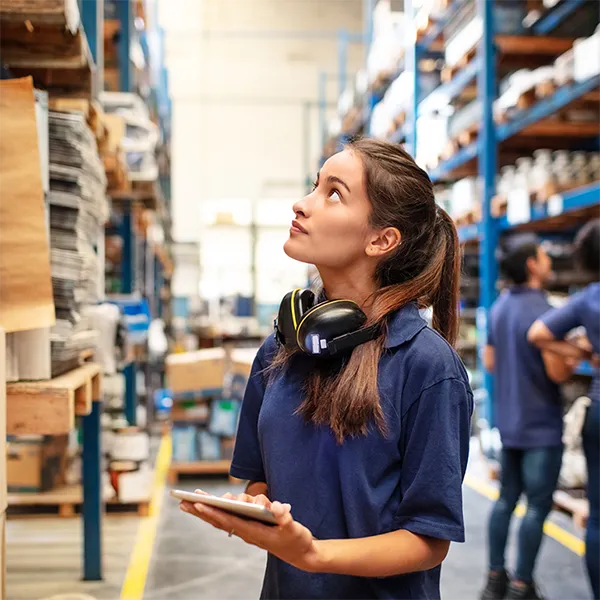 A worker in a warehouse surveying inventory while carrying a tablet.