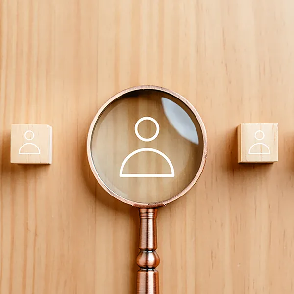 A magnifying glass on an icon of a person against a wood background.
