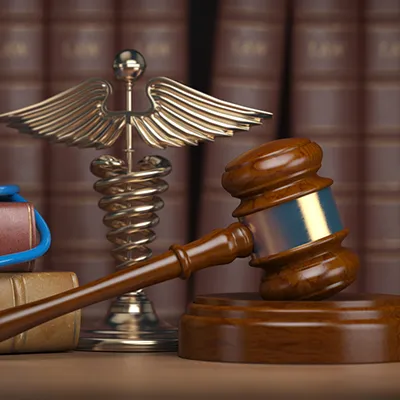 Legal volumes, a stethoscope, a medical caduceus, and a judges gavel on a desk.