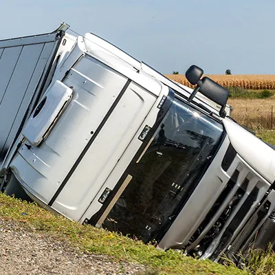 A crashed semi truck laying on it's side on the edge of a highway.
