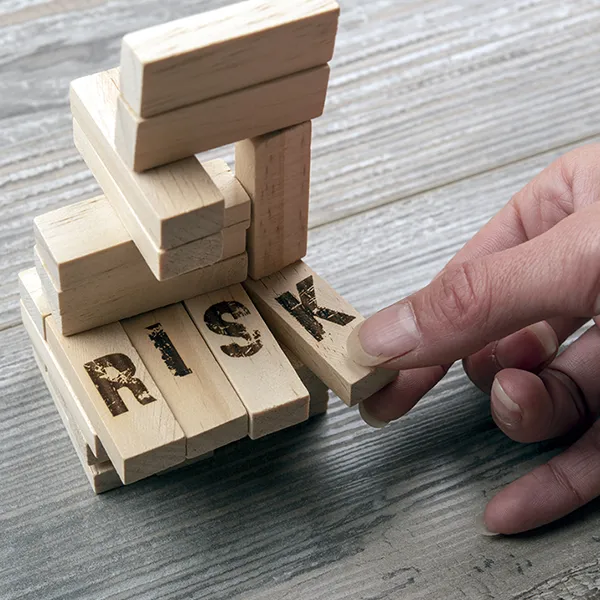 Someone about to knock over a tower of Jenga blocks. The blocks have 'RISK' written on them.
