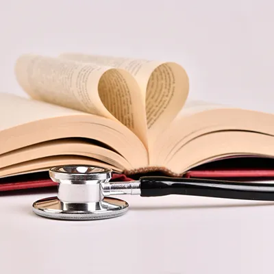 A stethoscope sitting on a white surface in front of an open book with two pages folded like a heart.