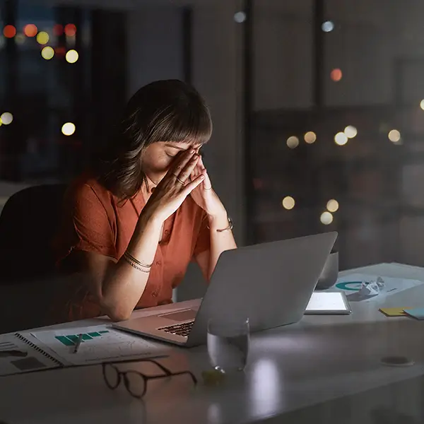 A woman sitting at her desk late at night, looking at a laptop computer.