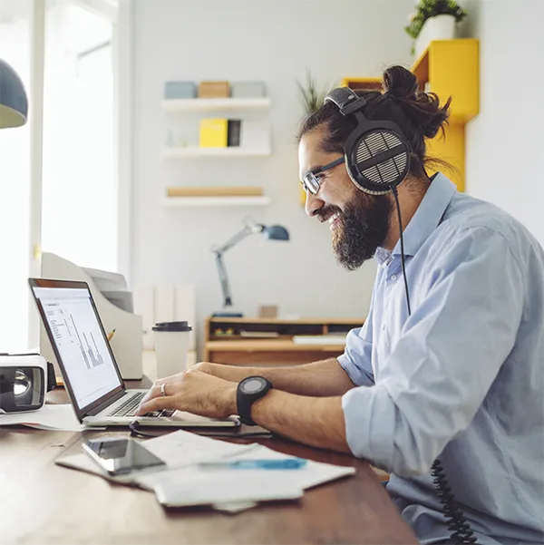 A man working from home at his laptop wearing over-ear headphones.
