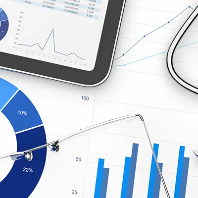 A pen, glasses, tablet, and stethoscope sitting across a background of charts and graphs.