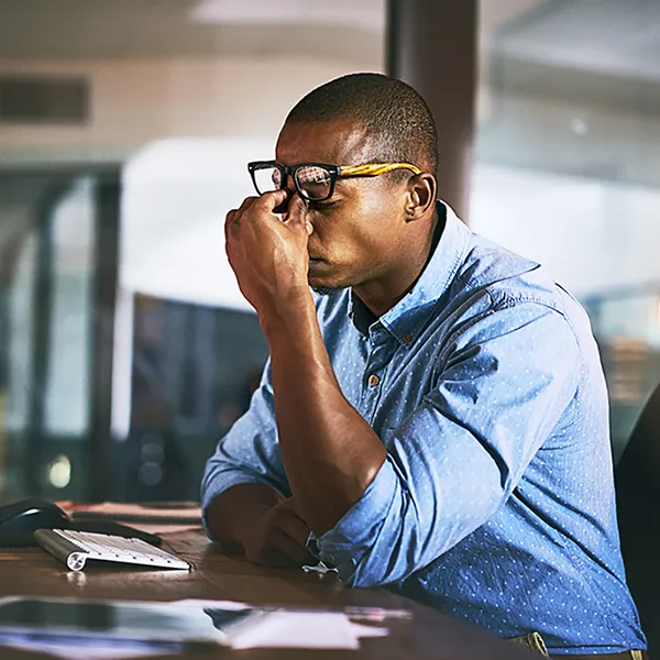 A professional at a computer pinching their forehead in stress.