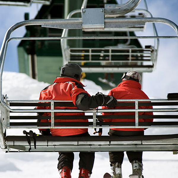 A pair of skiers wearing red jackets riding on a ski lift.