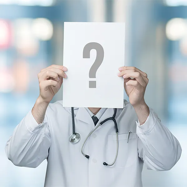 A medical professional holding a piece of paper with a question mark on it in front of their face.