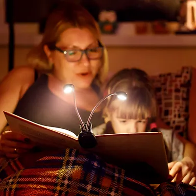 A mother reading a book to her child with the aid of electric book lights.