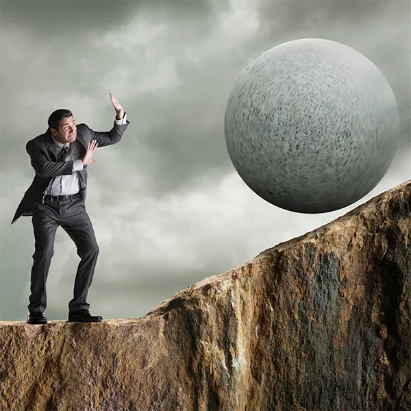 A man wearing a suit holding up his hands as a large boulder rolls towards him.