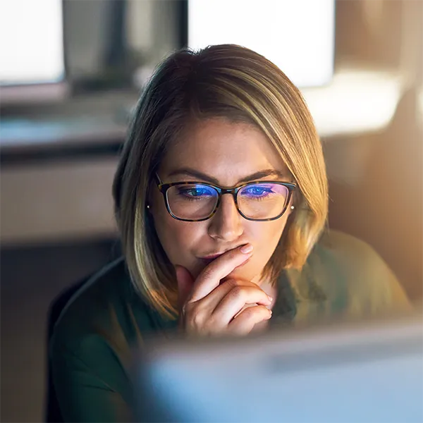 A woman looking pensively at her computer screen.