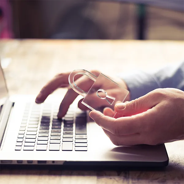 A person typing on a laptop computer. They're holding a transparent lock.