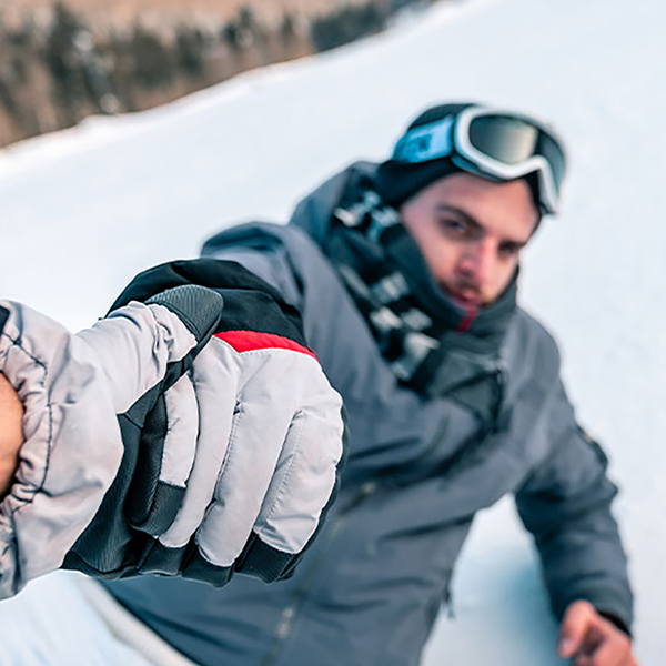 A person helps up a fallen snowboarder.