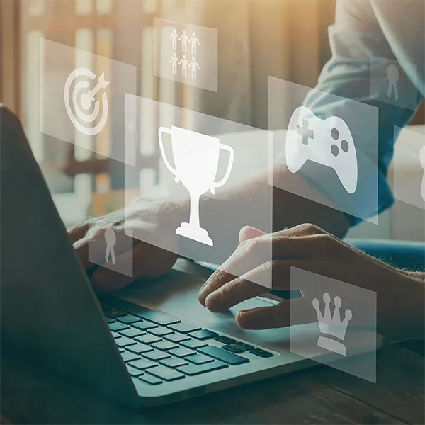 A persons hands on a laptop with gaming icon images floating above in the air.