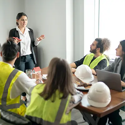 A safety meeting with workers in yellow vests sitting at a table