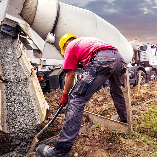 A contractor digging as a concrete truck pours out concrete.