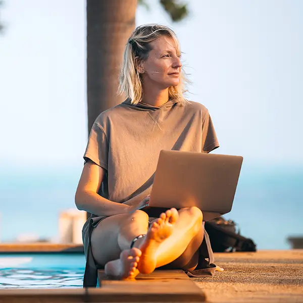 A person sitting beside a pool while working on their laptop computer.