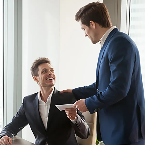 One professional hands paperwork to another while clapping him on the shoulder.