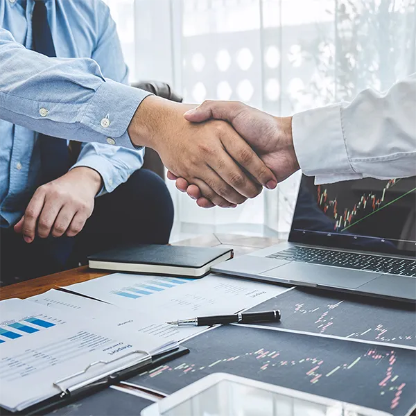 Two people shaking hands in front of a laptop featuring a report.