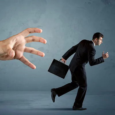 A business man carrying a briefcase and running from a large arm that is reaching out.