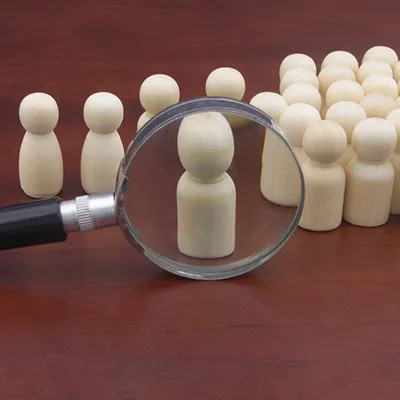 A magnifying glass sitting on a wood surface with chess pawns lined up behind it.
