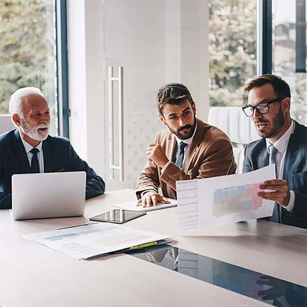 Three professionals wearing suits review a report.