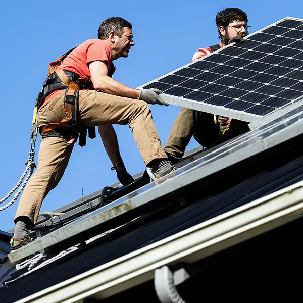 Two contractors install solar panels on the roof of a house.