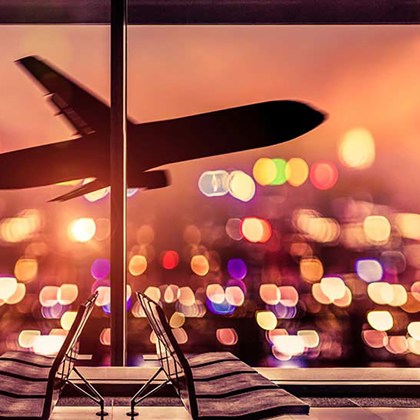 An airplane in flight seen from the window of an airport waiting area at night.