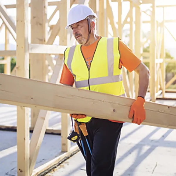 A construction worker wearing safety gear carrying a wooden beam.