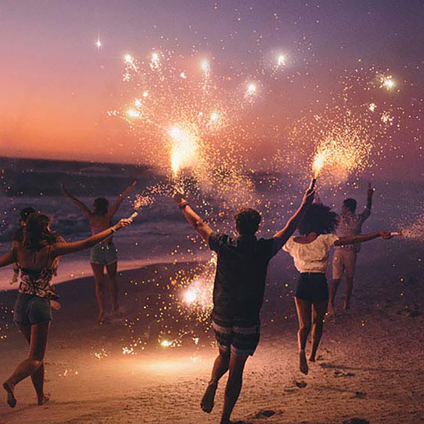 A group of people running down the beach waving sparklers.