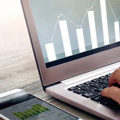 A laptop computer and phone sitting on a desk. Both are displaying bar charts on their screens.