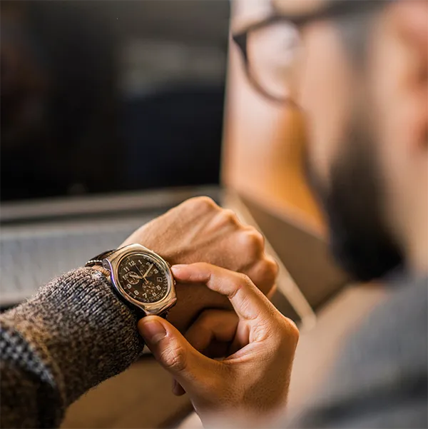 A remote worker looking at their laptop and checking their watch.