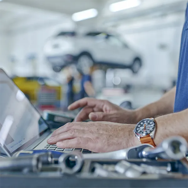 A person typing on their laptop computer surrounded by tools.