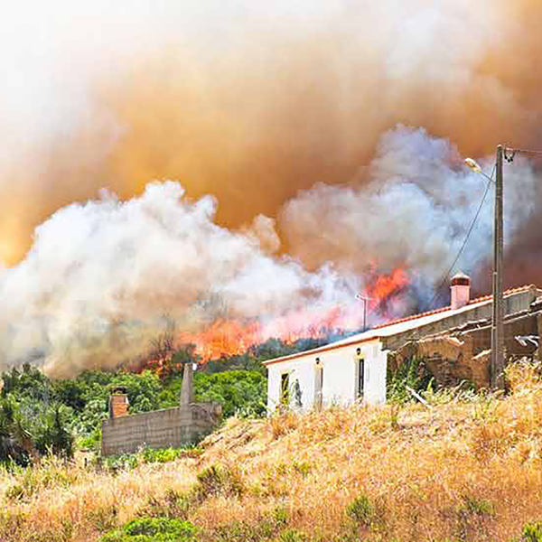 A home on a hillside with a wildfire in the background.
