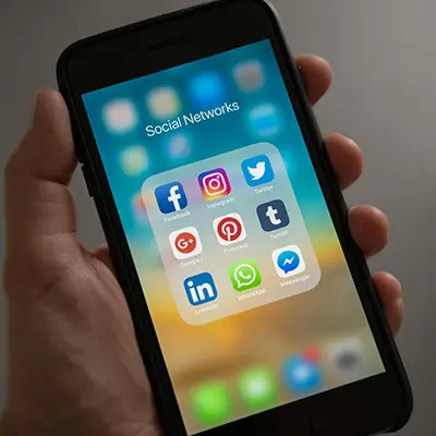 A mobile phone in a person's hand displaying social media app icons.