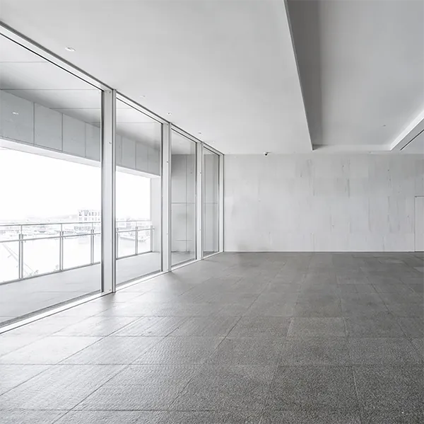 The concrete interior of a vacant building with large windows and stairs.