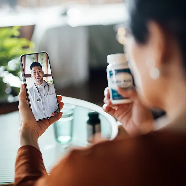 A person on a video call with their doctor, holding a bottle of medication.