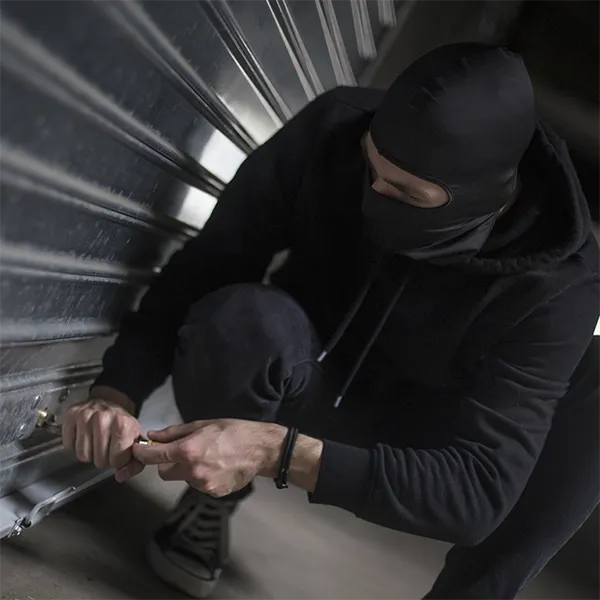 A thief breaking into a silver garage door.